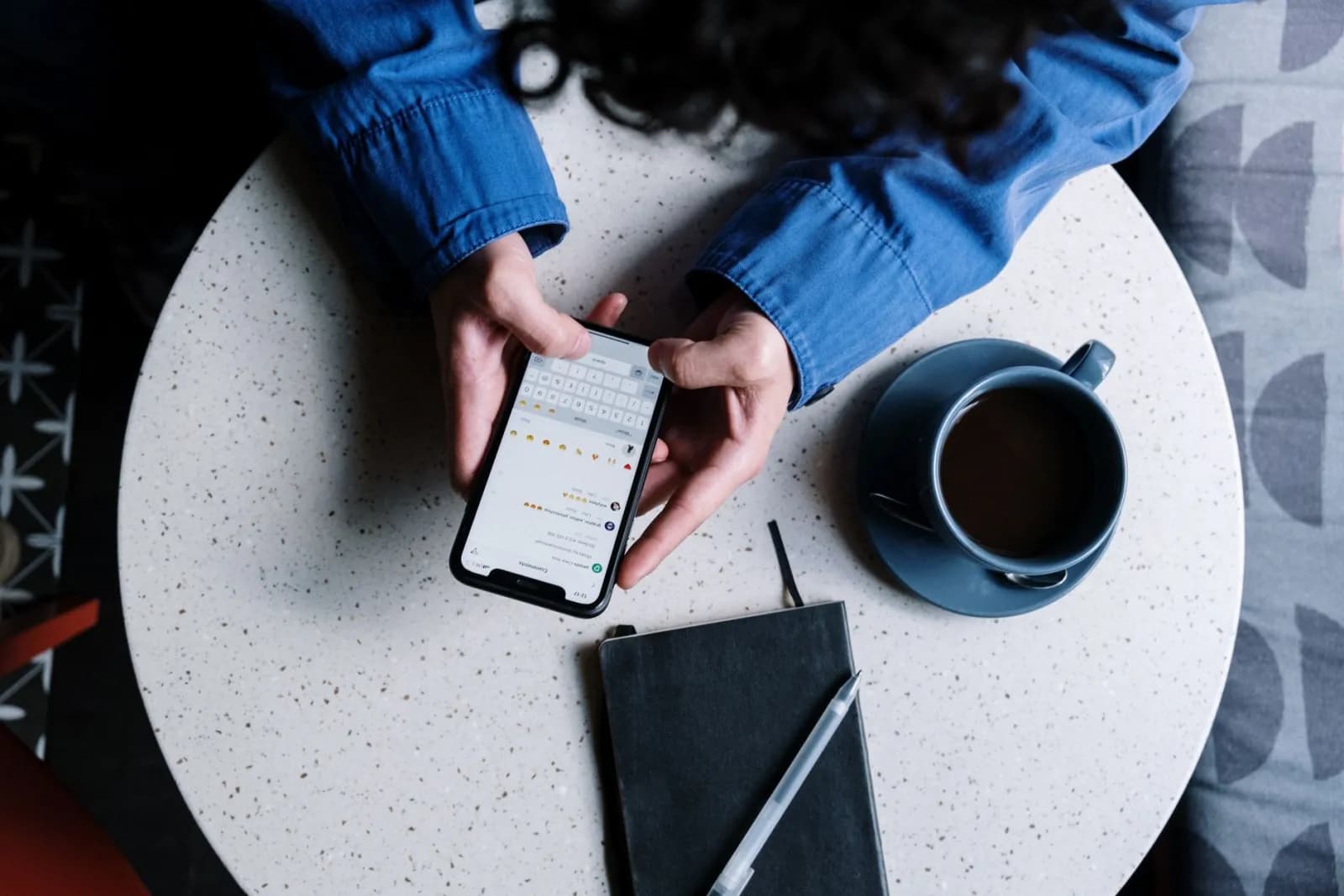 En person kollar mobilen under fikapausen vid ett cafébord