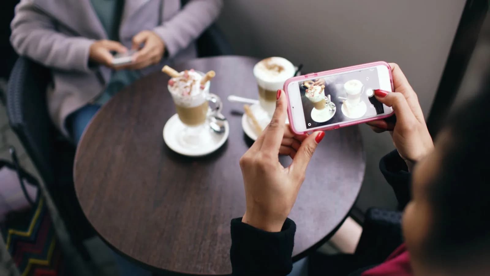 Två kvinnor på ett kafé fotograferar sitt kaffe med mobilen