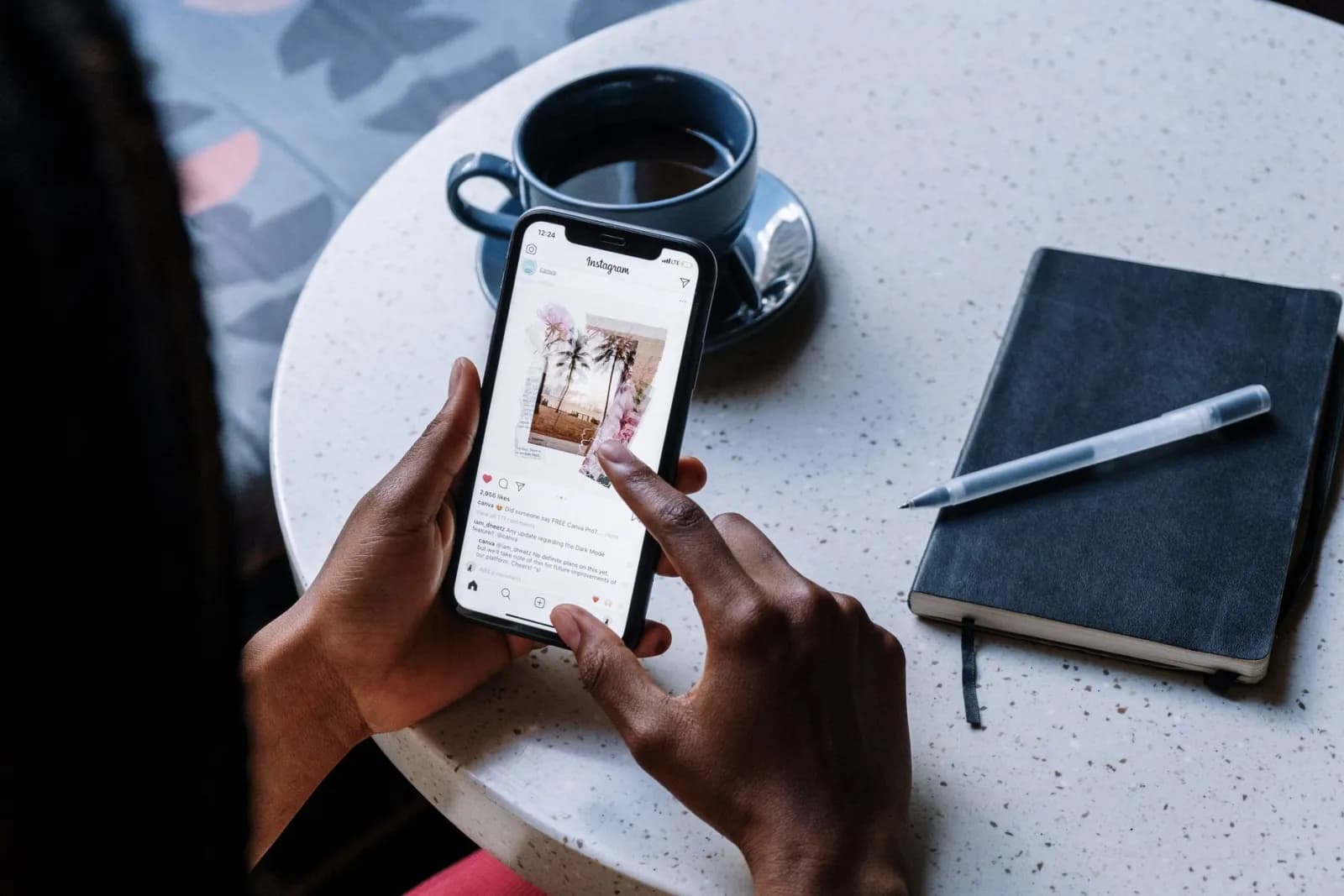 Hands holding a phone at a café table with coffee and a notebook