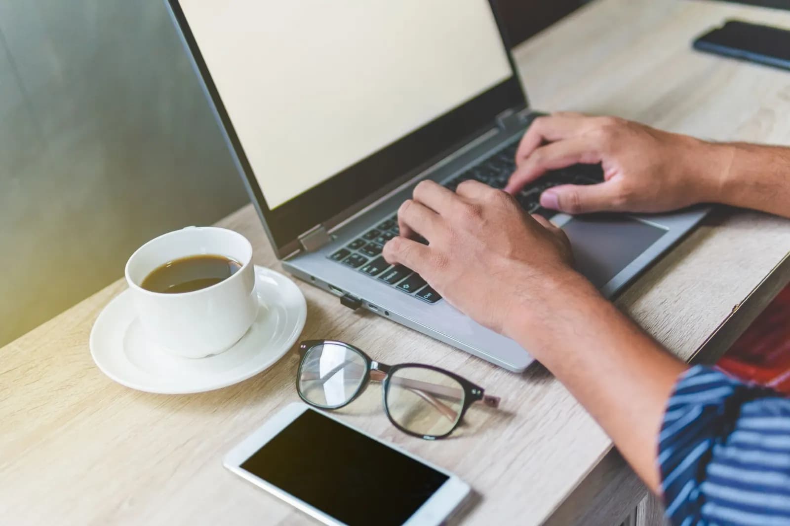 A person typing on a laptop at a desk with a cup of coffee