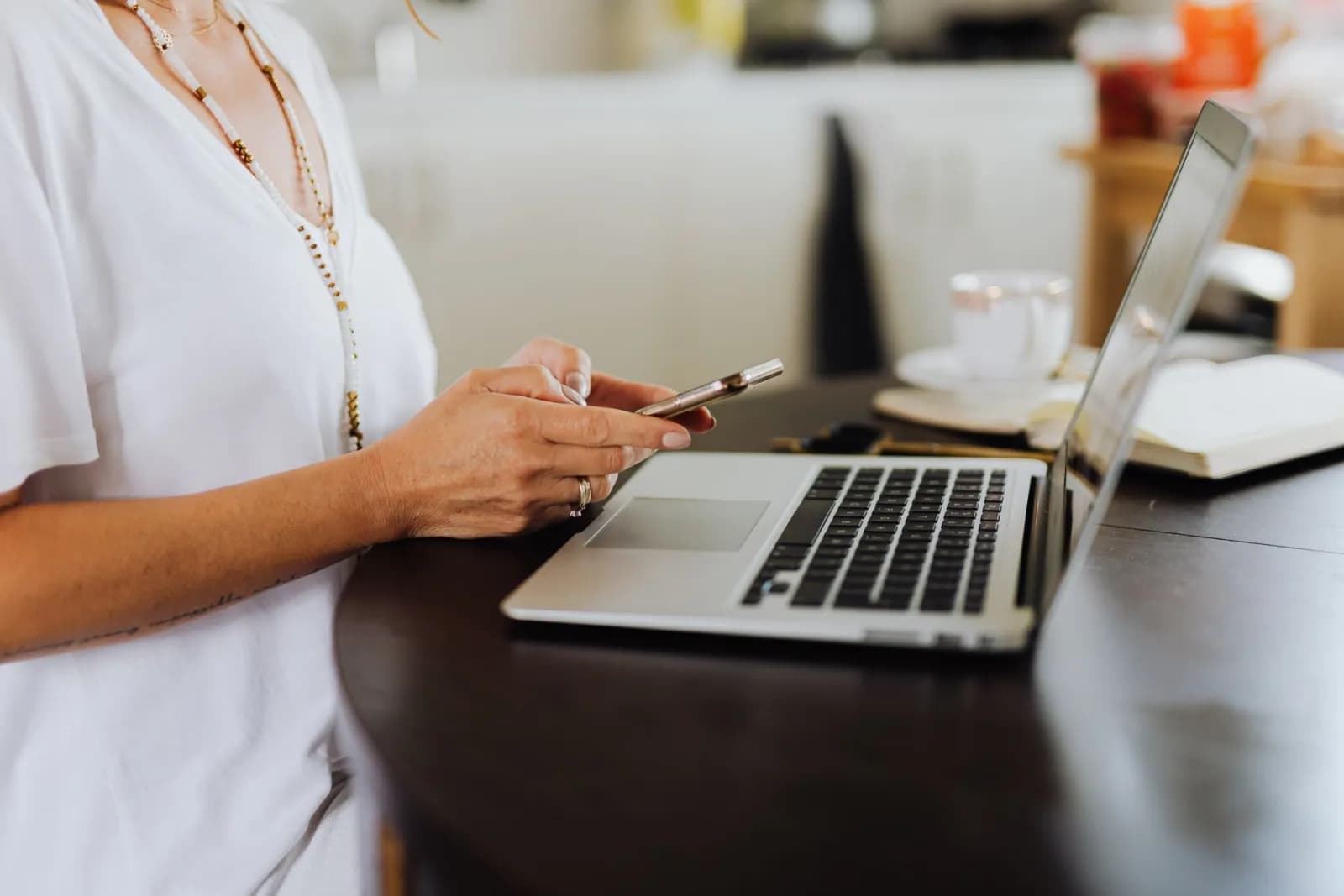 A woman using her phone and laptop at a home office desk